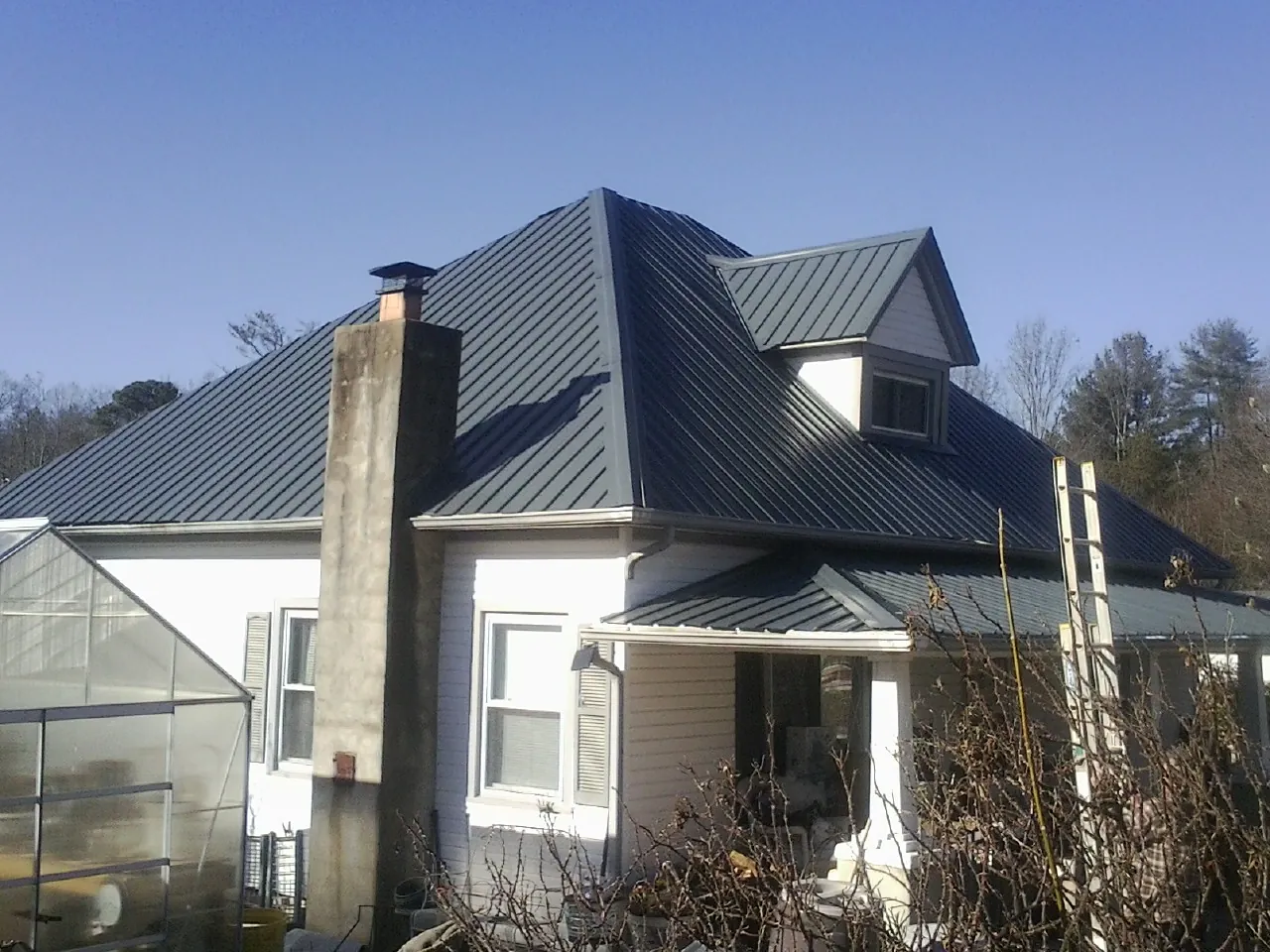 Dark blue standing seam metal roof on a white farmhouse with dormer — Slate & Tile Roof Repair by Roofing Brothers in Stuart