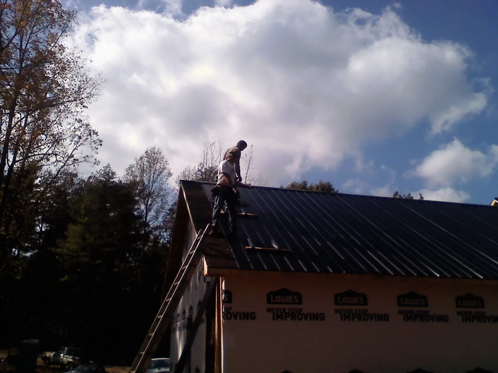 Roofer fastening dark metal panels high against a cloudy sky, from a Roof Inspection job in Stuart