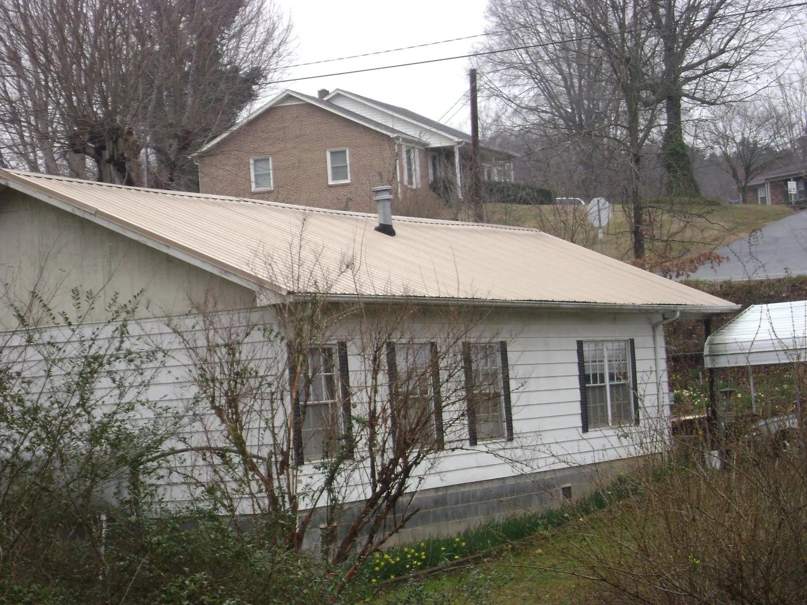 Tan metal roof on a white sided house set into a hillside — Commercial Roofing by Roofing Brothers in Stuart